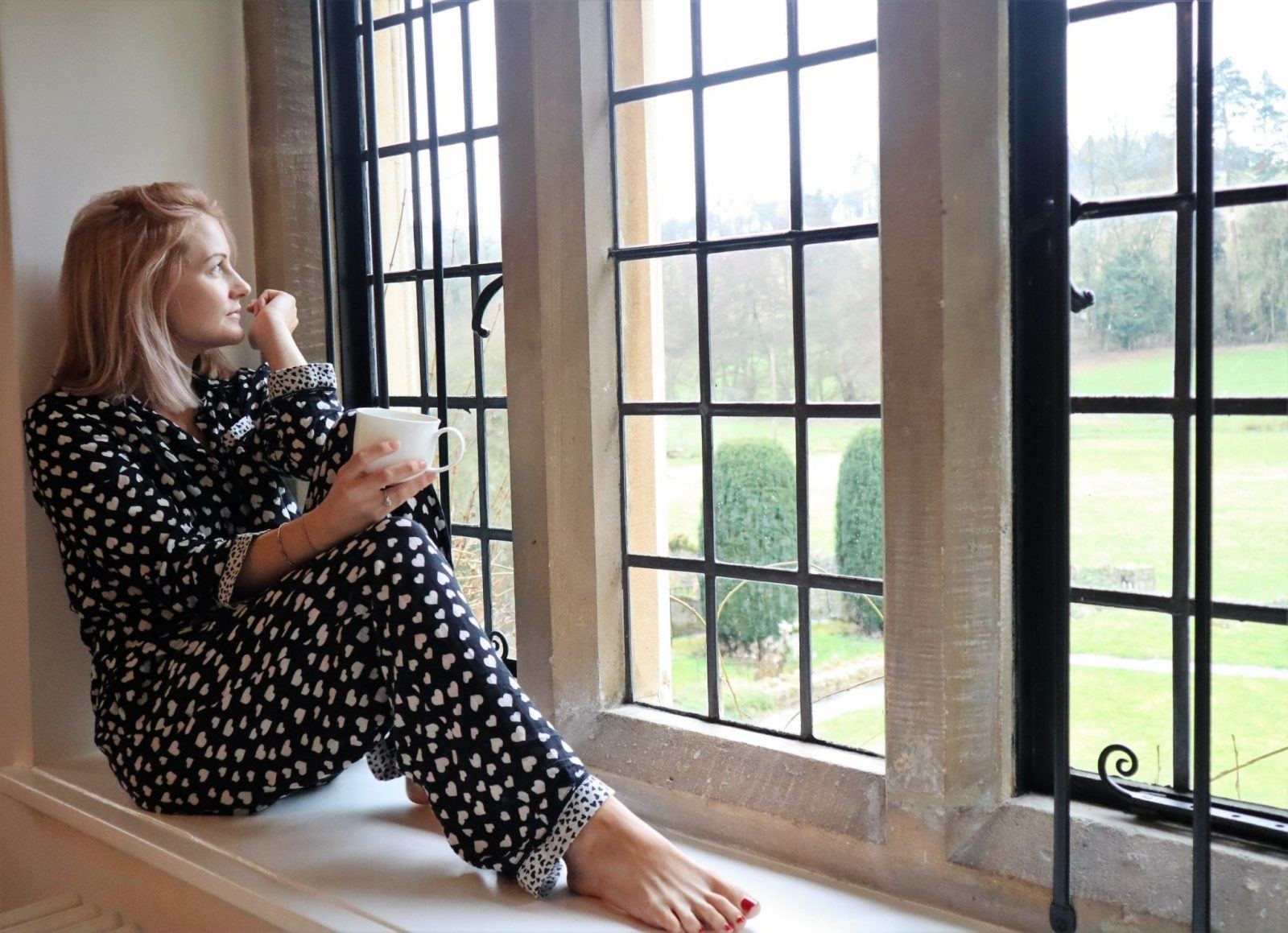 woman in pyjamas sat on a bay window looking out to the garden