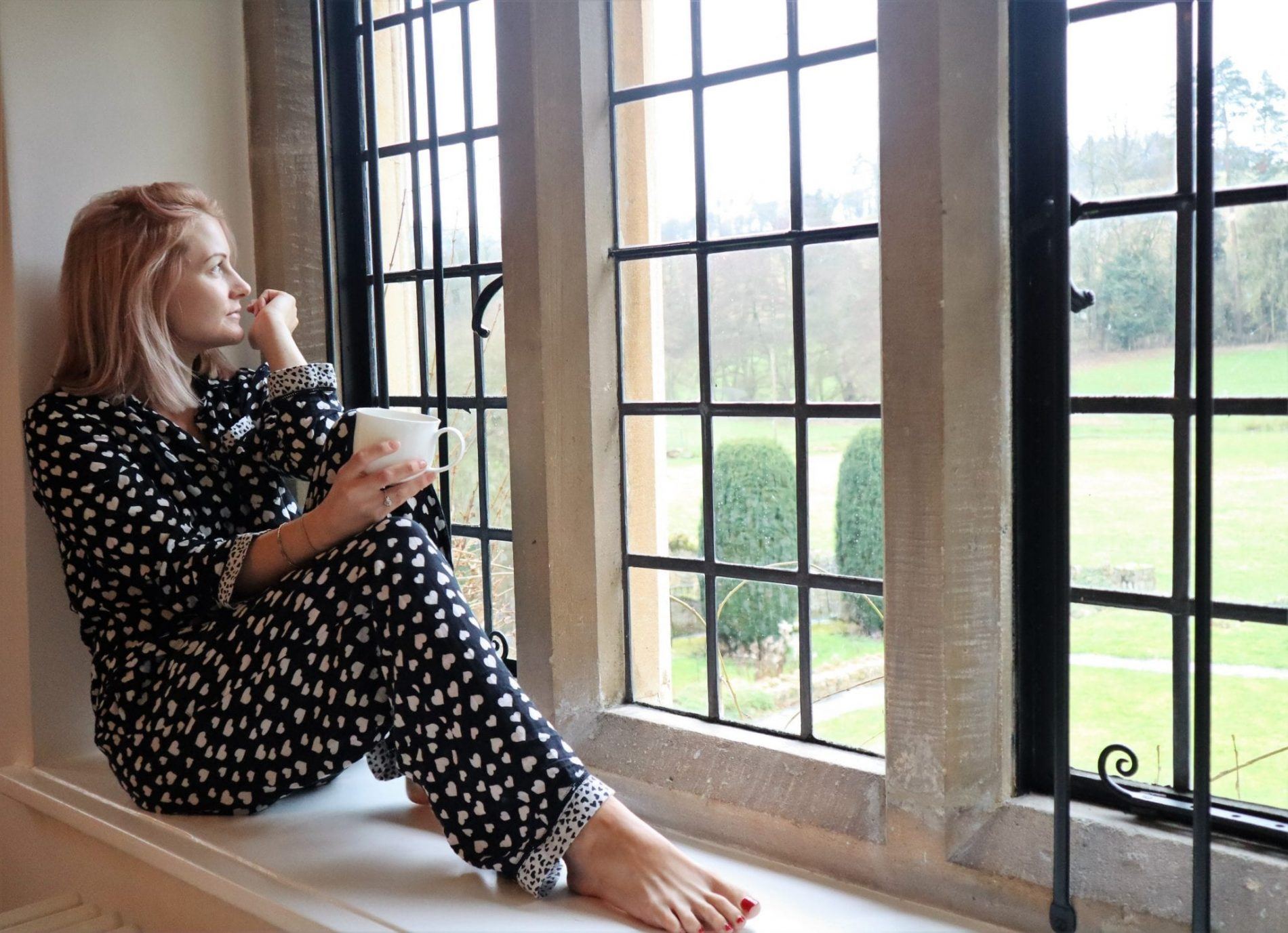 woman in pyjamas sat on a bay window looking out to the garden