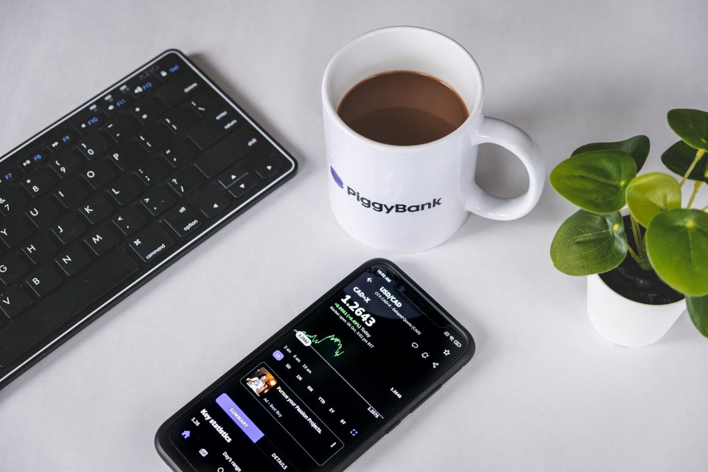 a close up of a budget tracker on a phone with a cup of coffee, representing the concept of compound interest UK