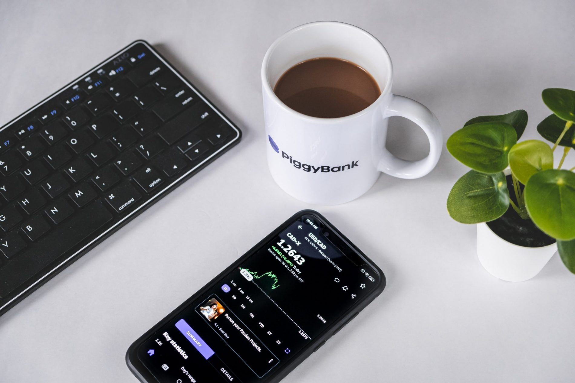 a close up of a budget tracker on a phone with a cup of coffee, representing the concept of compound interest UK