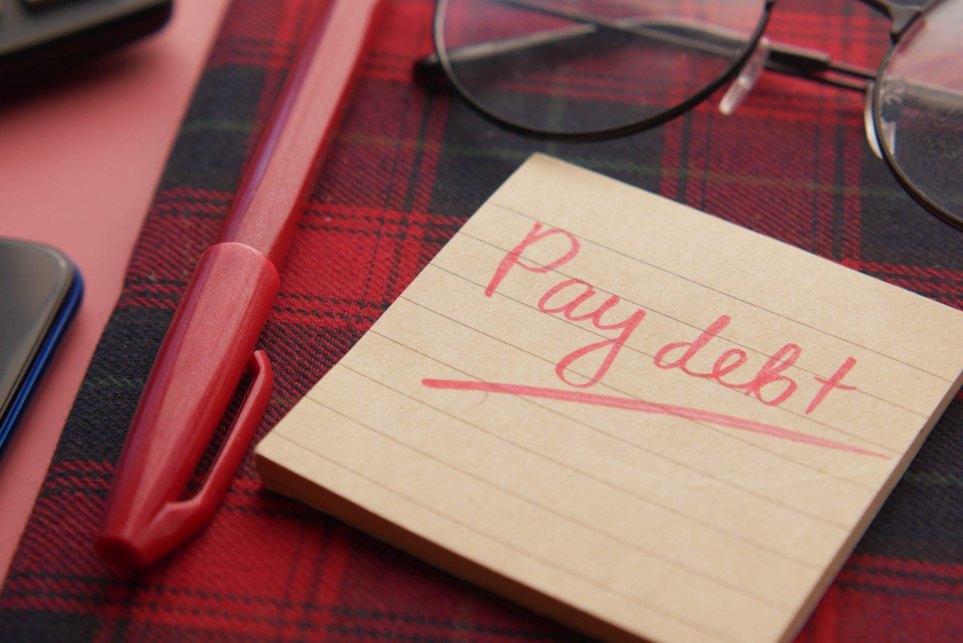 post it note with pay debt reminder to represent how to pay off debt and get better with finances